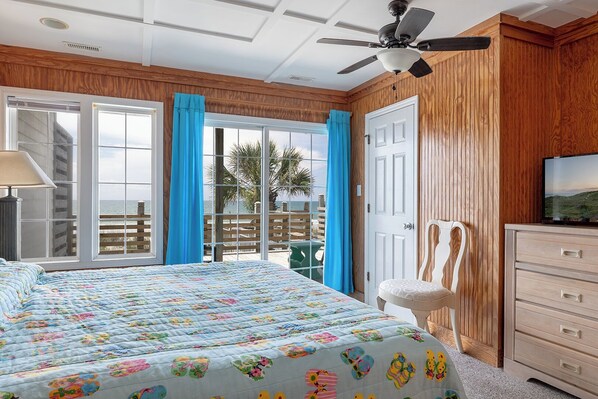 A bedroom with a bed, a TV, a dresser, and a balcony with a view of the ocean. - Aurora West, Oceanfront Duplex in Emerald Isle, NC! (Emerald Isle)