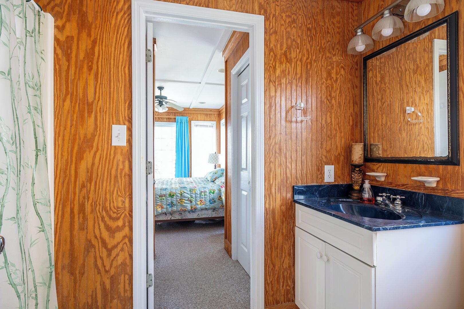 A bedroom with a bed, a bathroom with a sink and mirror, and a hallway with wooden walls.