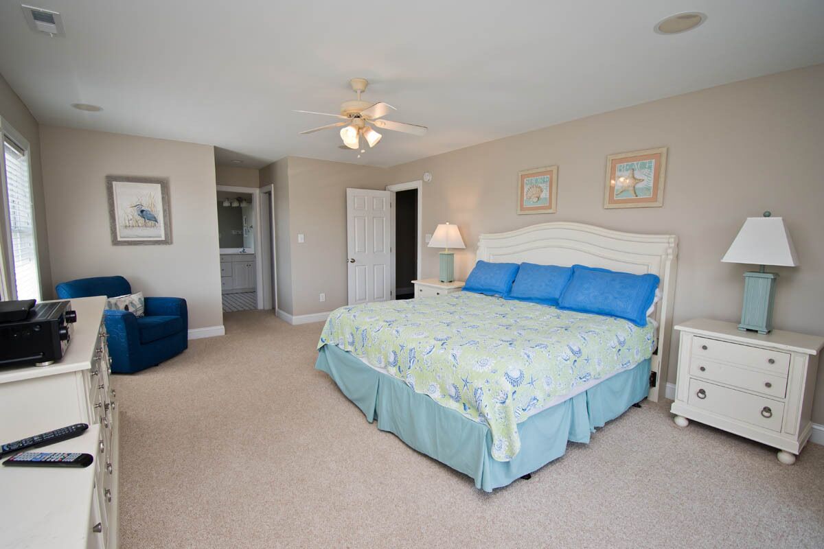 A bedroom with a bed, a desk, a chair, a nightstand, and a ceiling fan.