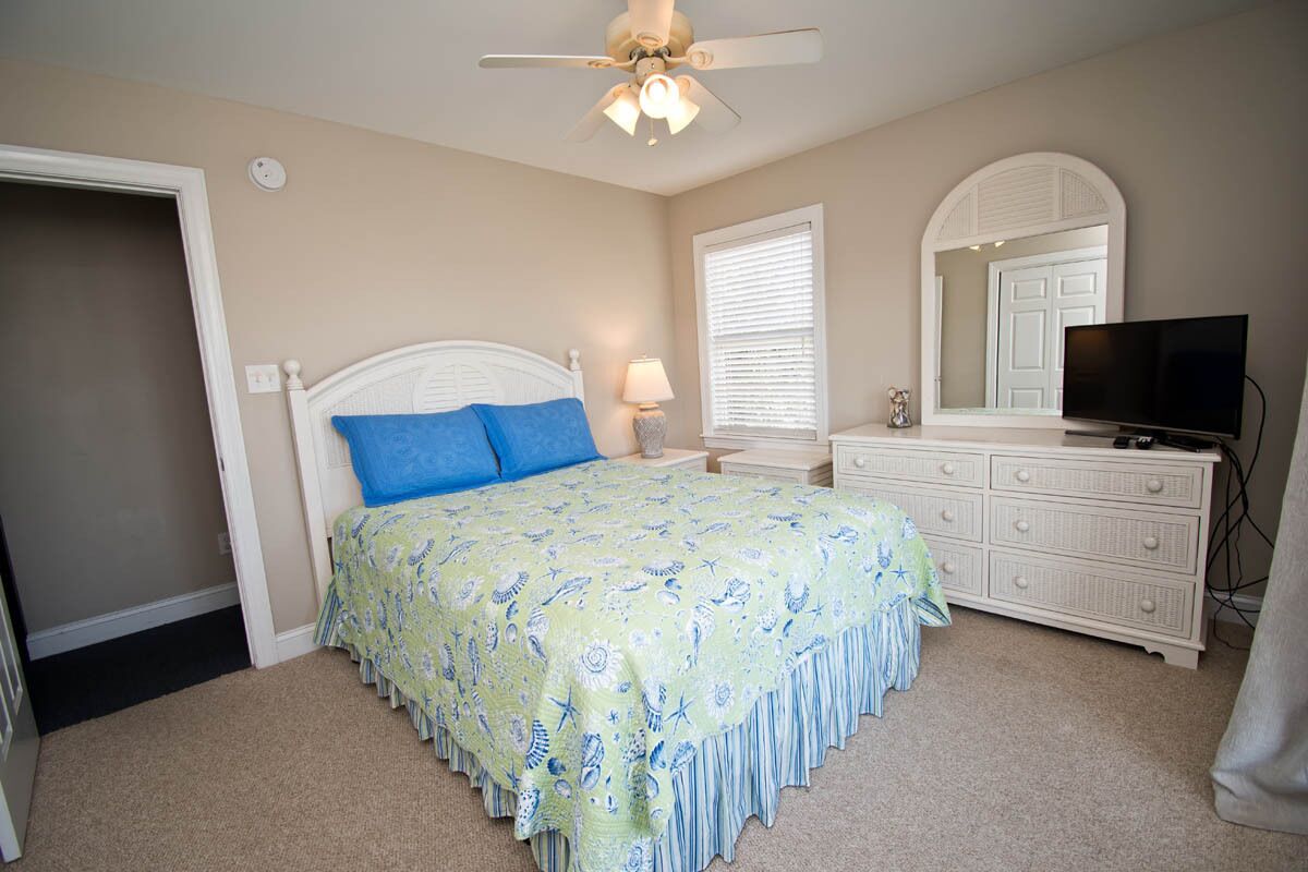 A bedroom with a bed, a dresser, a television, and a ceiling fan.