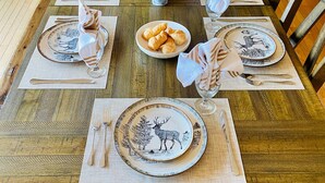 Una mesa de madera para comer, con platos, cubiertos y servilletas, rodeada de sillas.