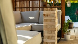 Une structure en bois dans un jardin, un canapé avec des coussins et des plantes en pot.