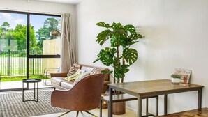 A modern living room with a sofa, a dining table, and a large plant. - Urban Pulse Townhouse with parking (Auckland South)