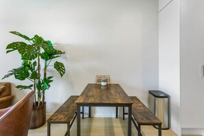 Un espace repas comprenant une table en bois, des bancs, une plante en pot et une poubelle.