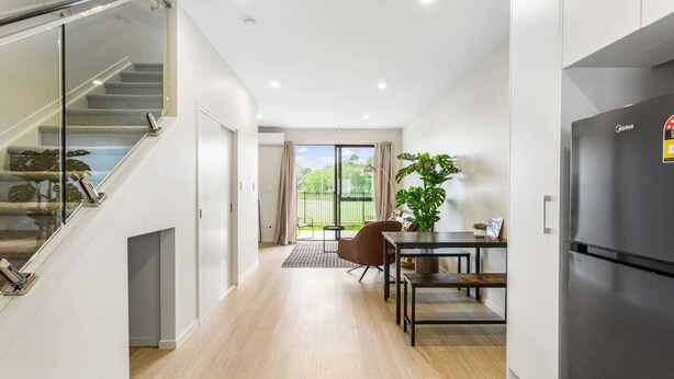A modern kitchen with a built-in refrigerator, a dining area with a table and chairs, and a staircase with glass railings. - Urban Pulse Townhouse with parking (Auckland South)