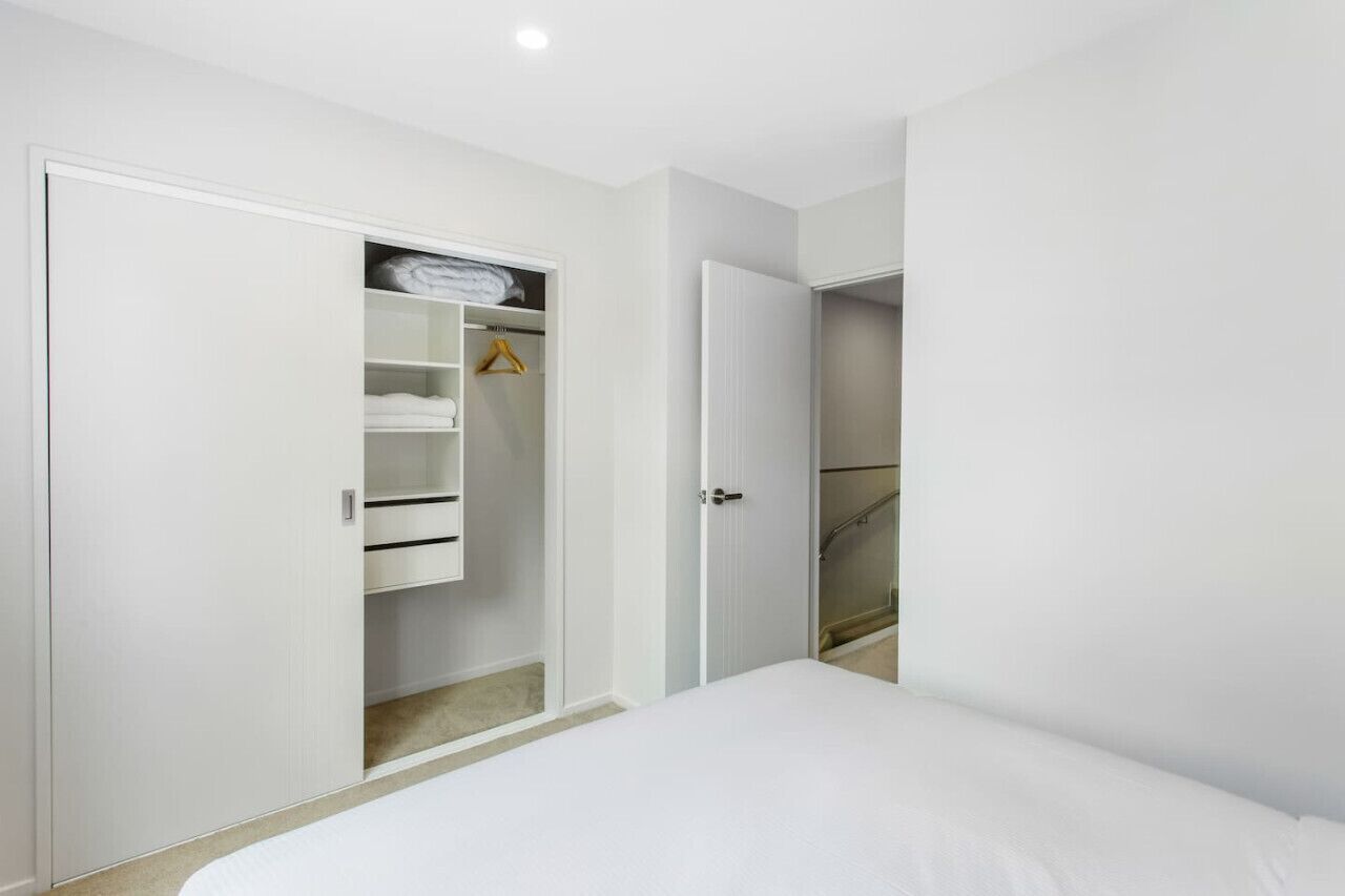 A bedroom with a bed, a closet with shelves and hanging space, and a door leading to another room.