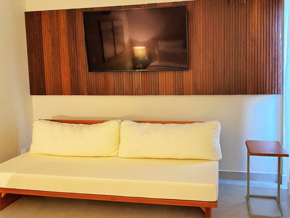 A modern hotel room with a wooden panel wall, a flat-screen TV mounted above a bed with white bedding. - Flat Ilê de Pipa Varanda - By Almare (Tibau do Sul)