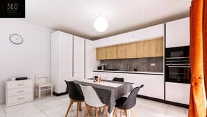 Une cuisine moderne avec des meubles blancs, une table à manger et quatre chaises, ainsi qu’un four encastré.