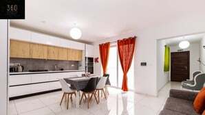 Une cuisine moderne avec des meubles blancs, une table à manger avec des chaises et des rideaux orange.