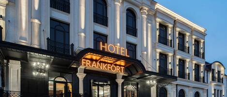 A grand hotel with a classic facade, large arched windows, and a prominent illuminated sign.
