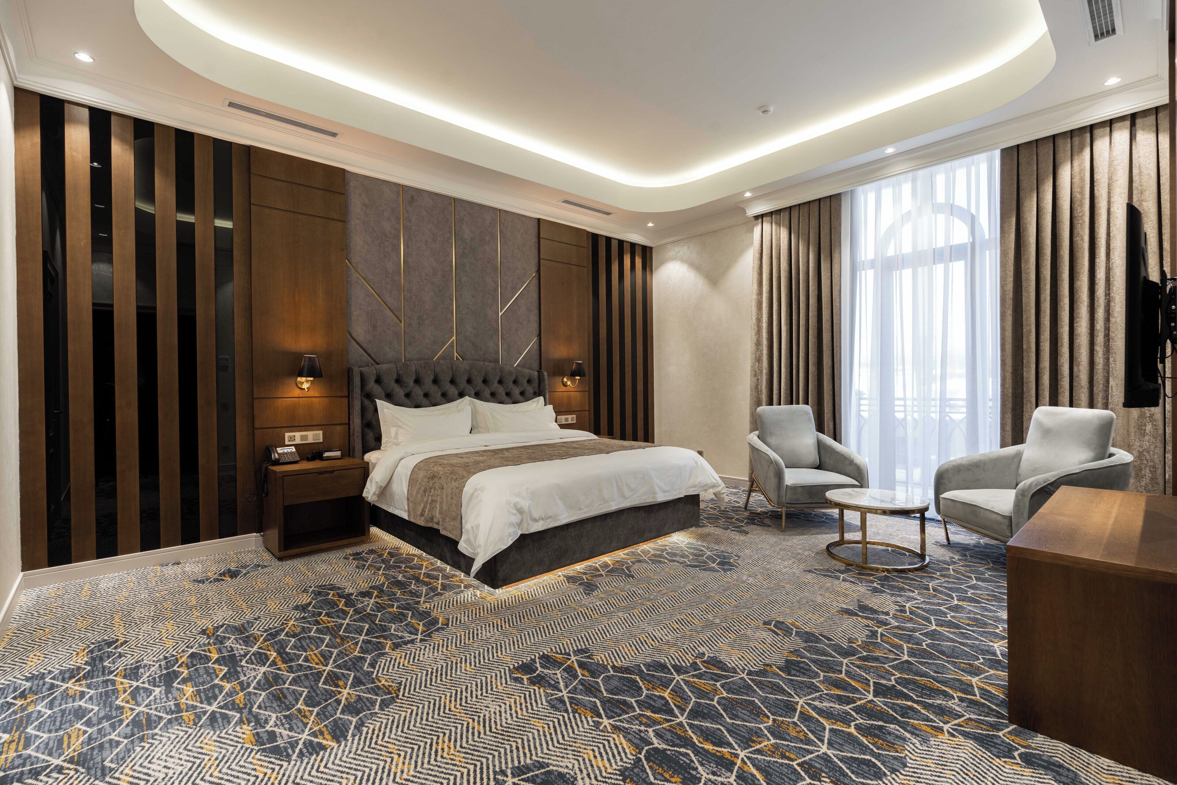 Una habitación de hotel moderna con una cama grande, dos sillones, una mesita y un televisor.