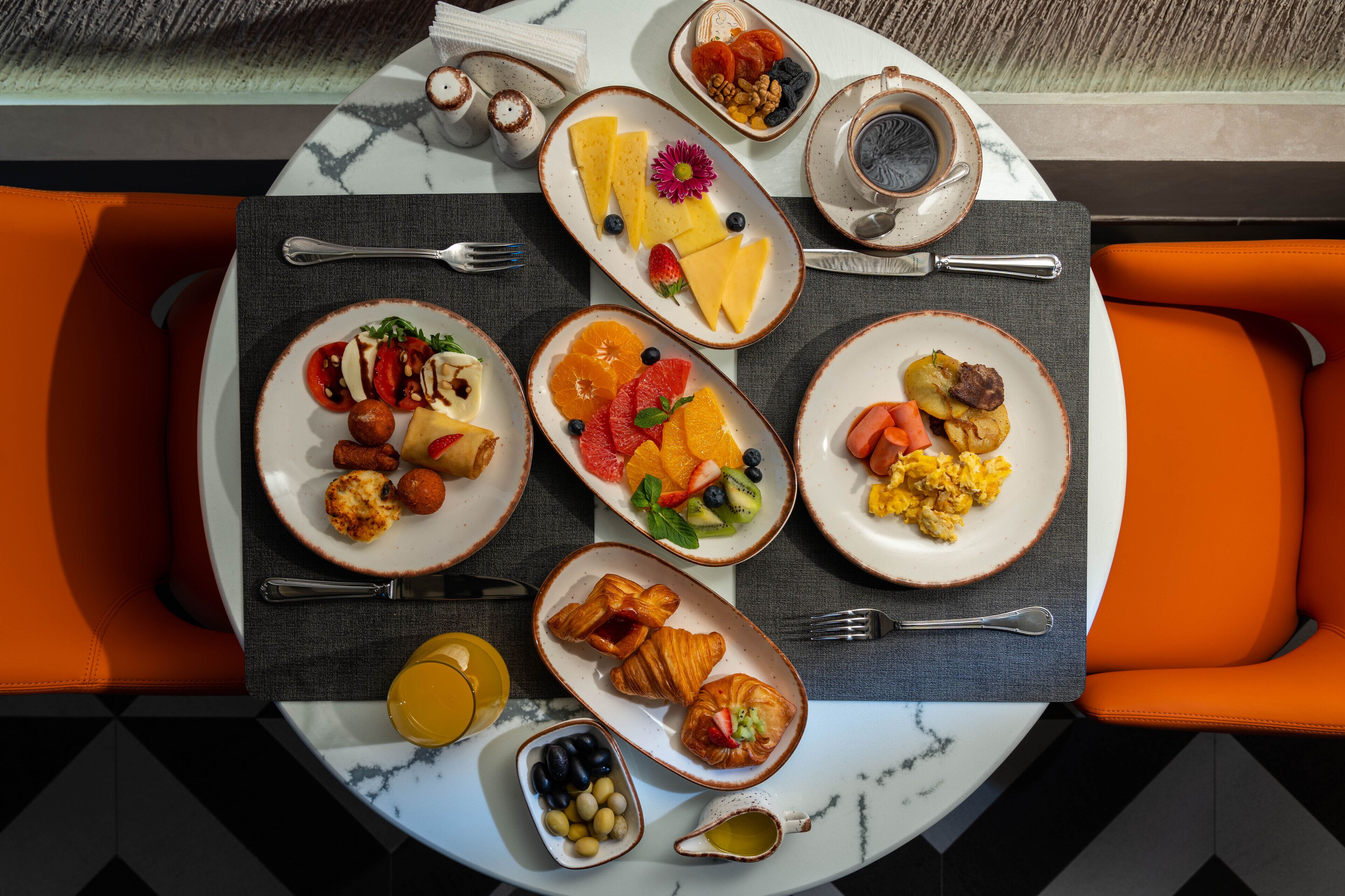 Une table de petit-déjeuner avec des assiettes remplies de nourriture, une tasse de café et des chaises orange.