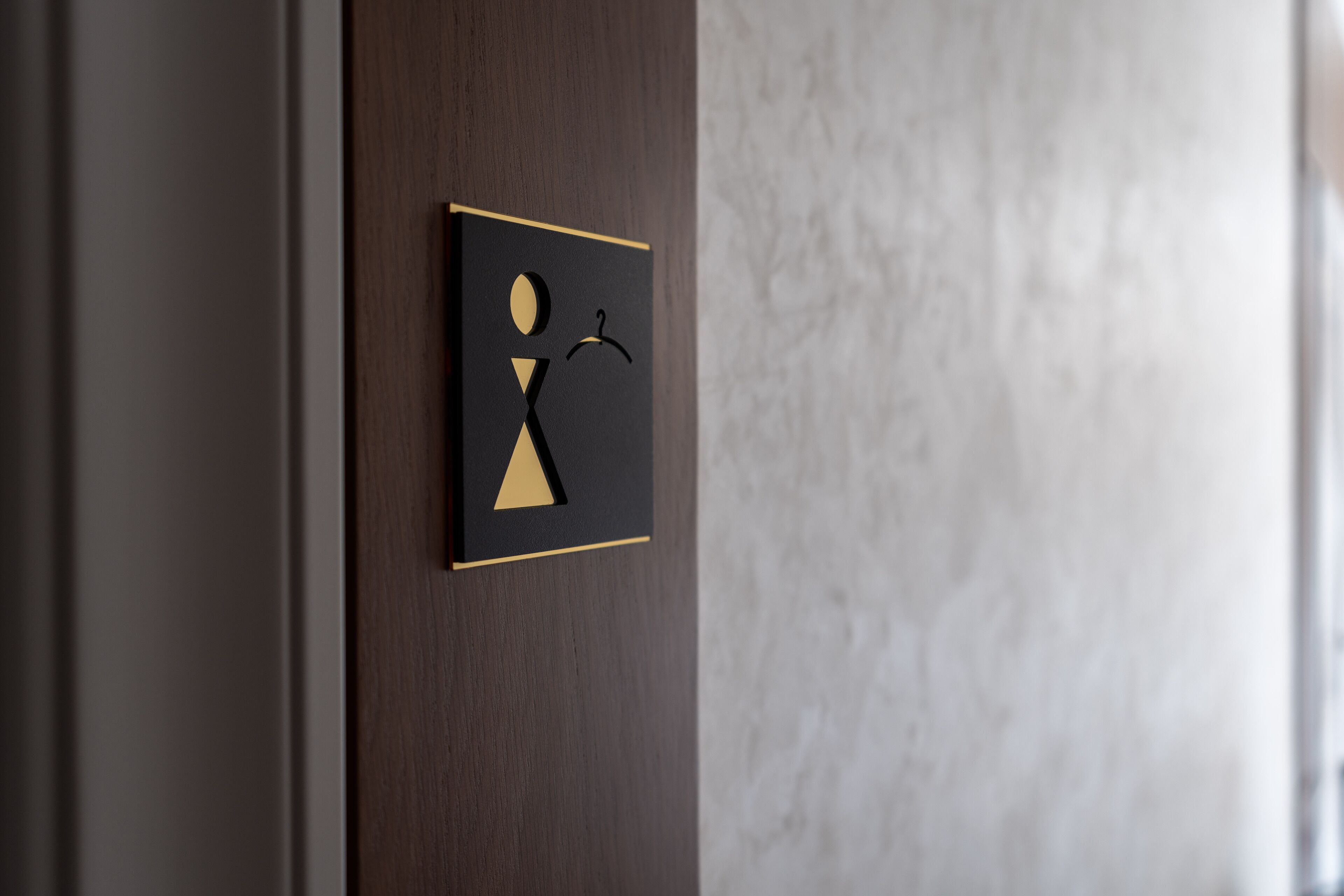 Porta com placa preta e dourada indicando um banheiro masculino.