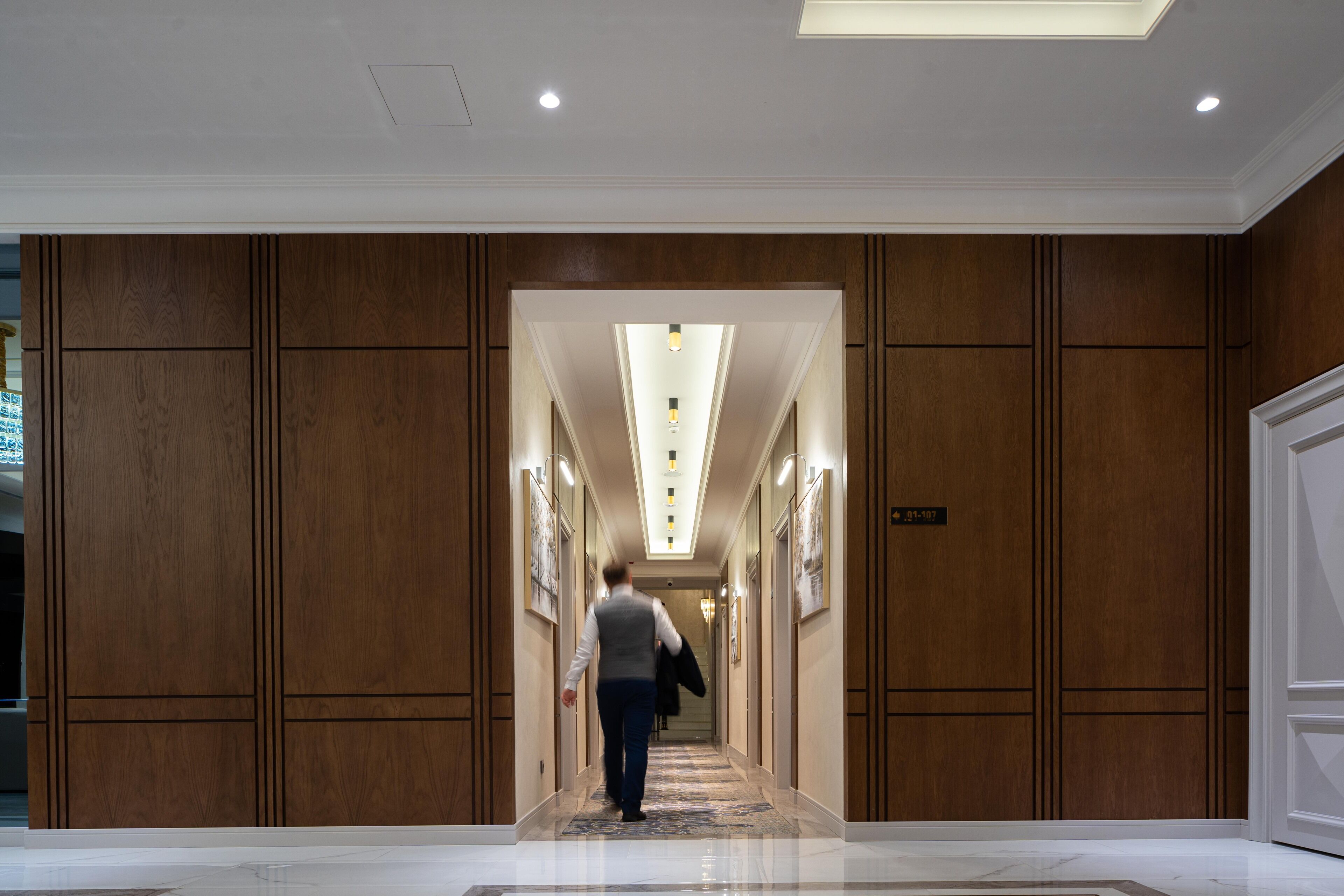 A hallway with wooden paneling and a polished floor, leading to a room with a sign indicating the room number.