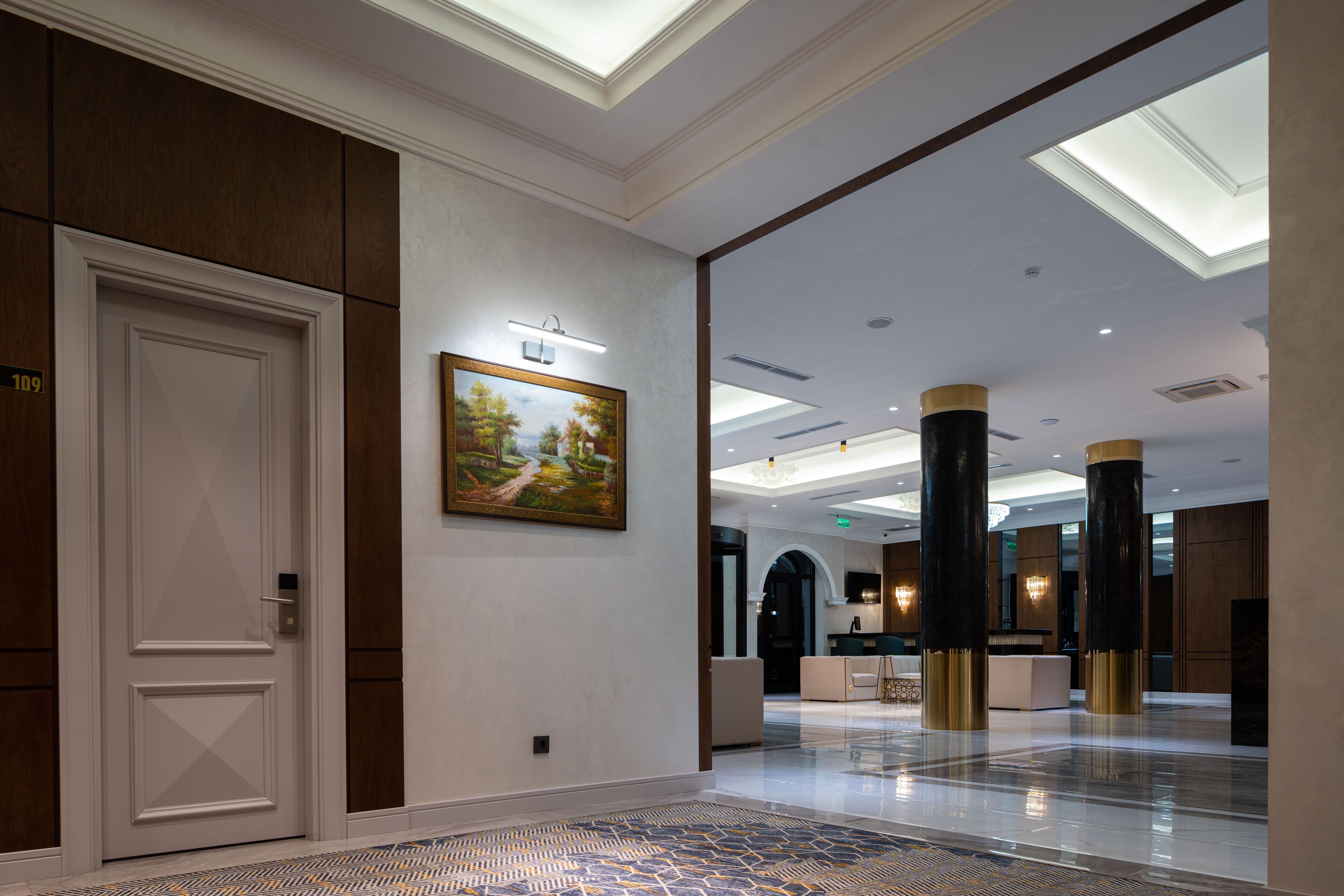 Een hotel lobby met een receptiebalie, een schilderij aan de muur en een deur met het nummer 109.