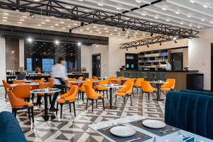 A modern restaurant with orange chairs and tables, a bar area, and a blue seating area.