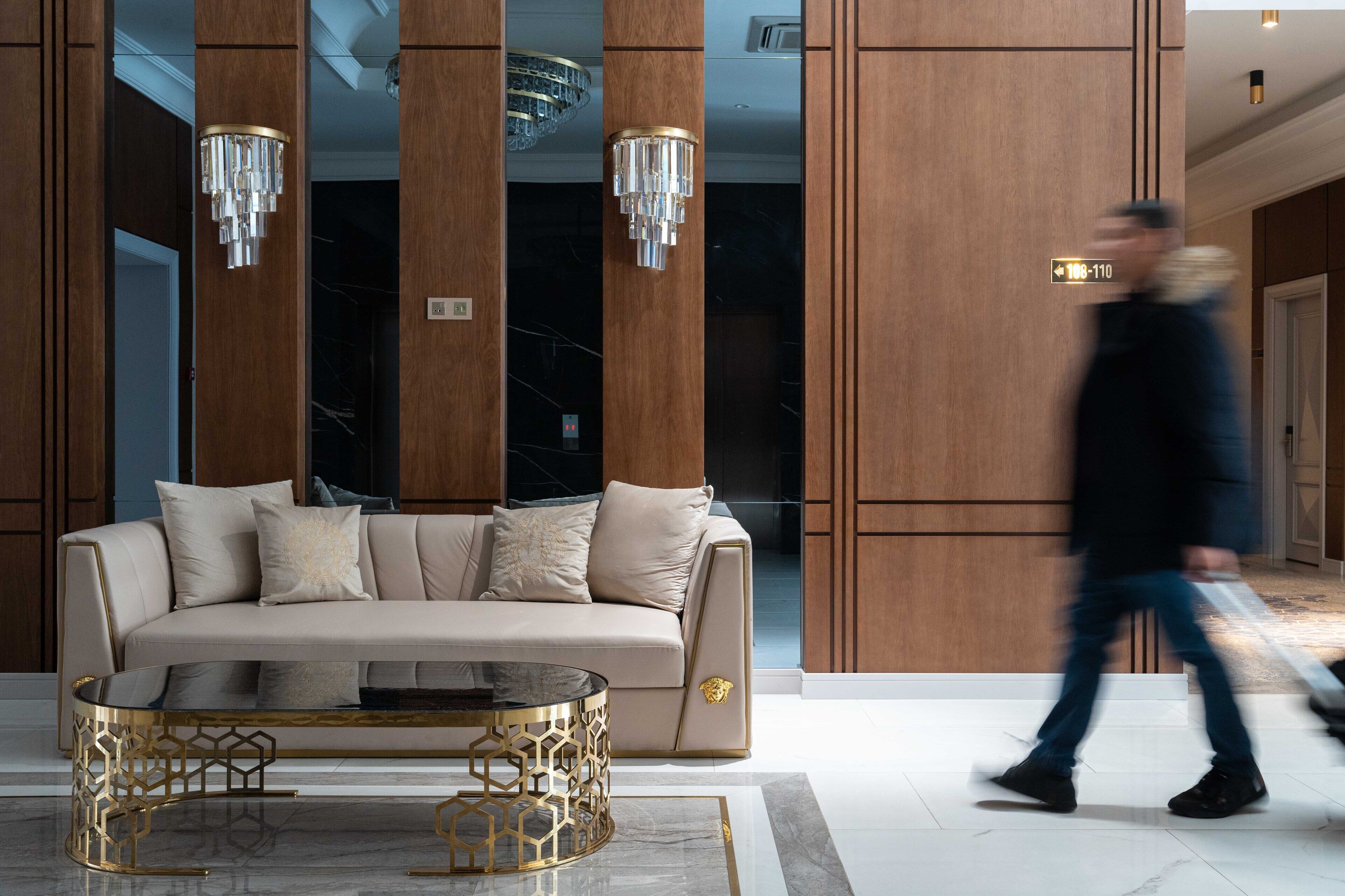 A modern lobby with a beige sofa, a glass coffee table, and two chandeliers.