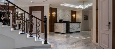A grand lobby with a marble staircase, a reception desk, and a chandelier.