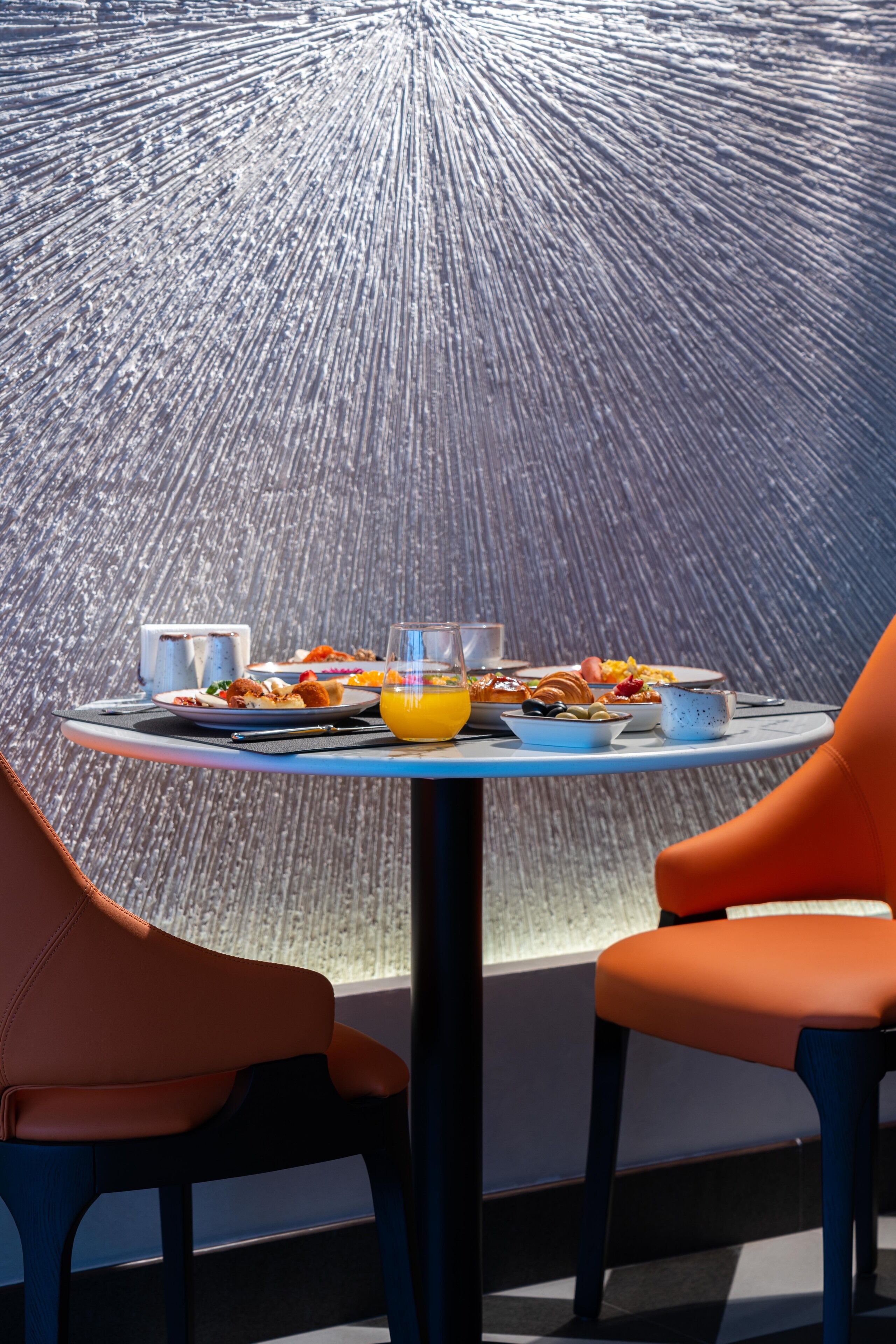 A dining table with breakfast items and two orange chairs.
