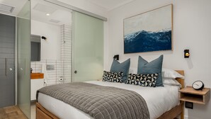 Een moderne slaapkamer met een groot bed, een douchecabine van glas, een houten nachtkastje en een wandklok.