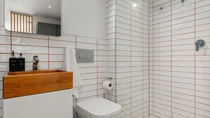 Een moderne badkamer met toilet, houten wastafelmeubel en een douchecabine met glazen wanden.