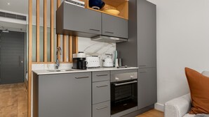 Een kleine keuken met grijze kastjes, een ingebouwde oven en een aanrecht met koffiezetapparaat en waterkoker.