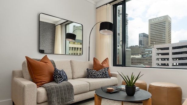 Een moderne woonkamer met een bank, een ronde salontafel en een stadsgezicht door grote ramen.
