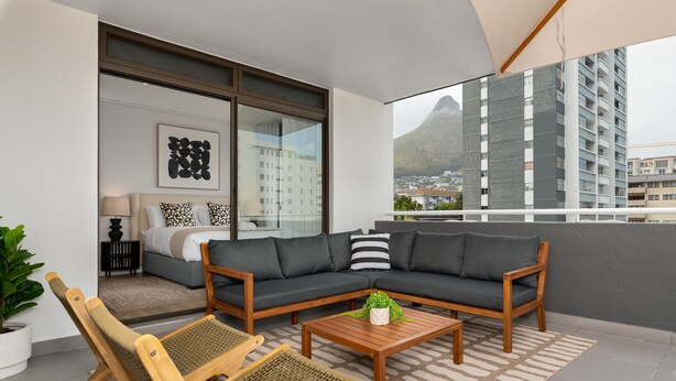 A balcony with a sofa, two wooden chairs, a coffee table, and a potted plant.