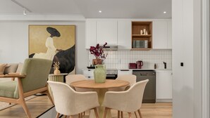 A modern kitchen with white cabinets, a microwave, and a stove. There is a dining area with a round table and chairs.
