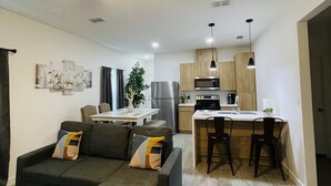 A modern living room with a dark green sofa, a ceiling fan, and a dining area with a bar. - New & Modern 2b/2b Apartment 
Centrally located   (Pharr)