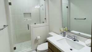 A modern bathroom with a glass-enclosed shower, a white sink with a wooden vanity, and a large mirror. - New & Modern 2b/2b Apartment 
Centrally located   (Pharr)