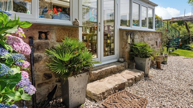 A cottage with a glass front, stone steps, and potted plants.