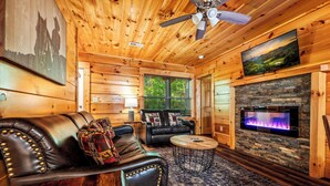 A cozy log cabin interior with a leather sofa, a fireplace, and a television mounted on the wall.