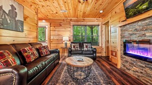A cozy cabin interior with a leather sofa, a round coffee table, and a stone fireplace.