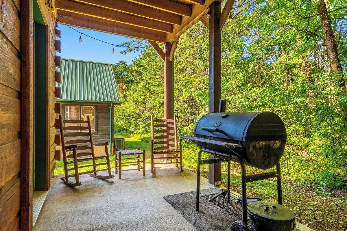 A covered outdoor patio with a grill, a rocking chair, and a small table.