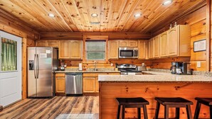 A kitchen with wooden cabinets, stainless steel appliances, a granite countertop, and a bar area with stools.