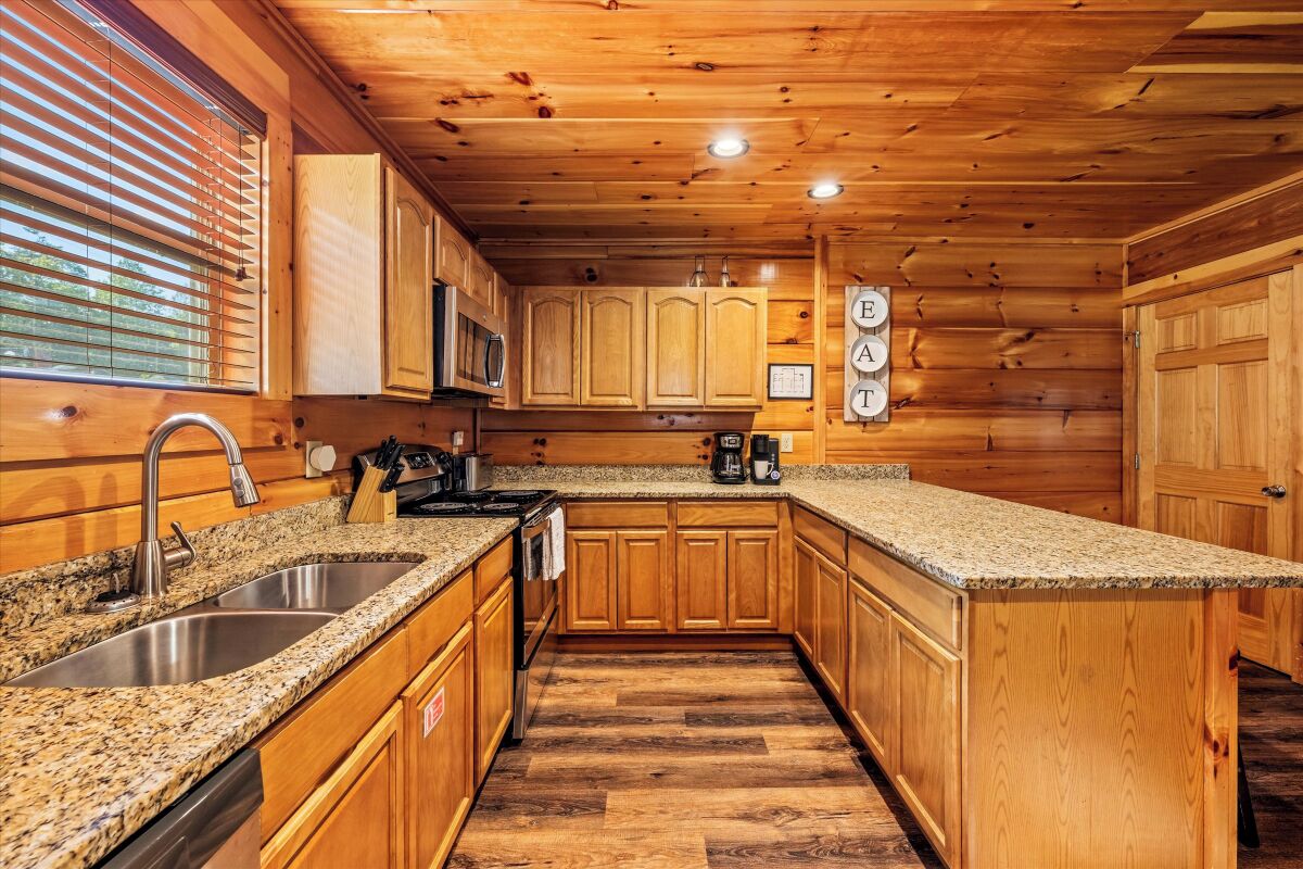 Una cocina con armarios de madera, encimeras de granito, fregaderos de acero inoxidable y un microondas.