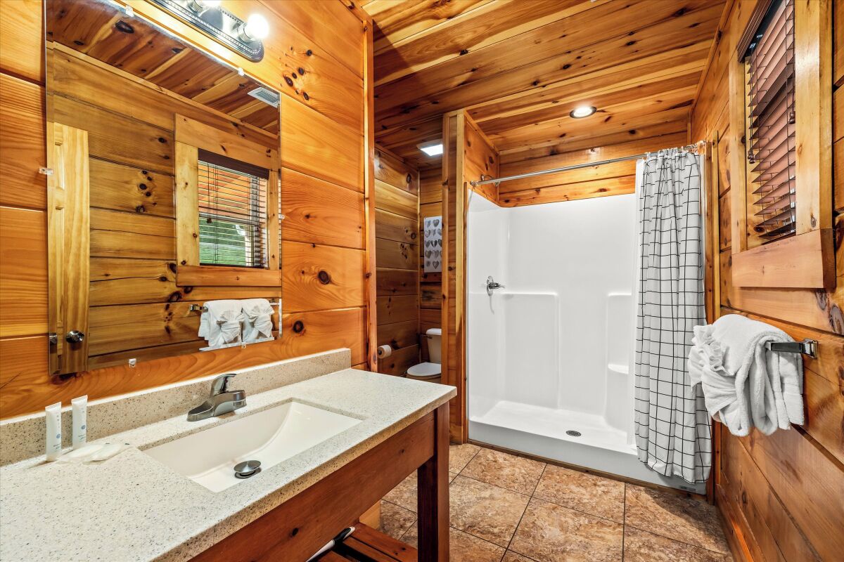 A wooden cabin bathroom with a double sink, a mirror, a shower, and a toilet.
