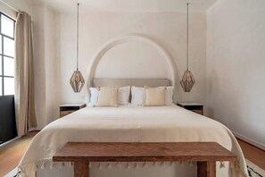 A bedroom with a large bed, a wooden bench, two nightstands, and a large arched window. - Superb house in Condesa with huge patio (Ciudad de México)