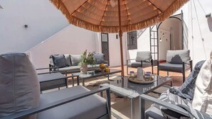 Un espace de détente extérieur moderne, doté d’un parasol en chaume, de fauteuils rembourrés et d’une table en verre.