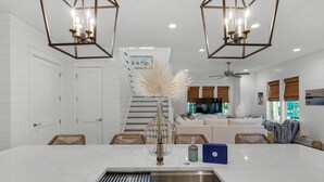 Una cocina moderna con una isla central, un comedor con sillas de mimbre y una sala de estar con sofá y televisor.