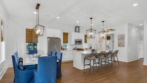 Una cocina moderna con muebles blancos, electrodomésticos de acero inoxidable y sillas tapizadas en azul.