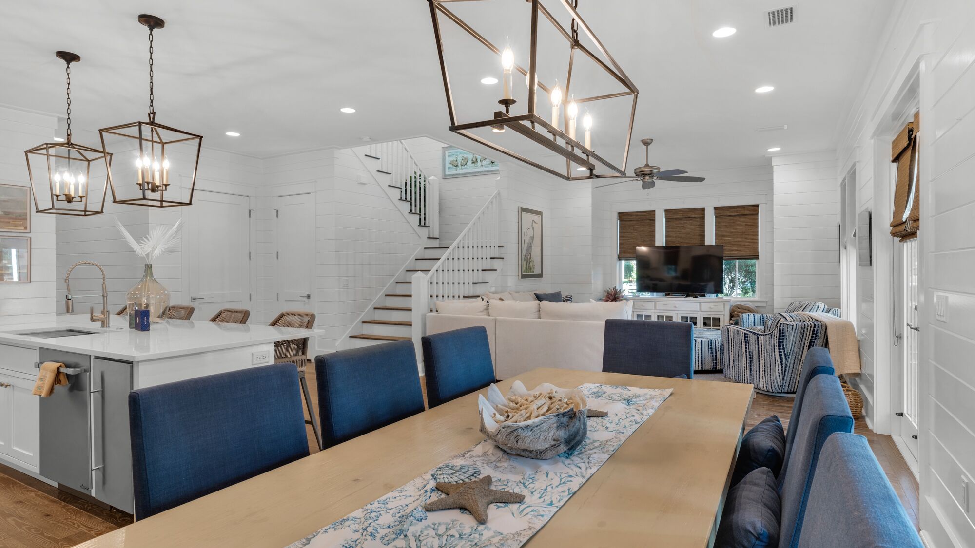A spacious living area with a central island, blue upholstered seating, and a staircase leading to an upper level.