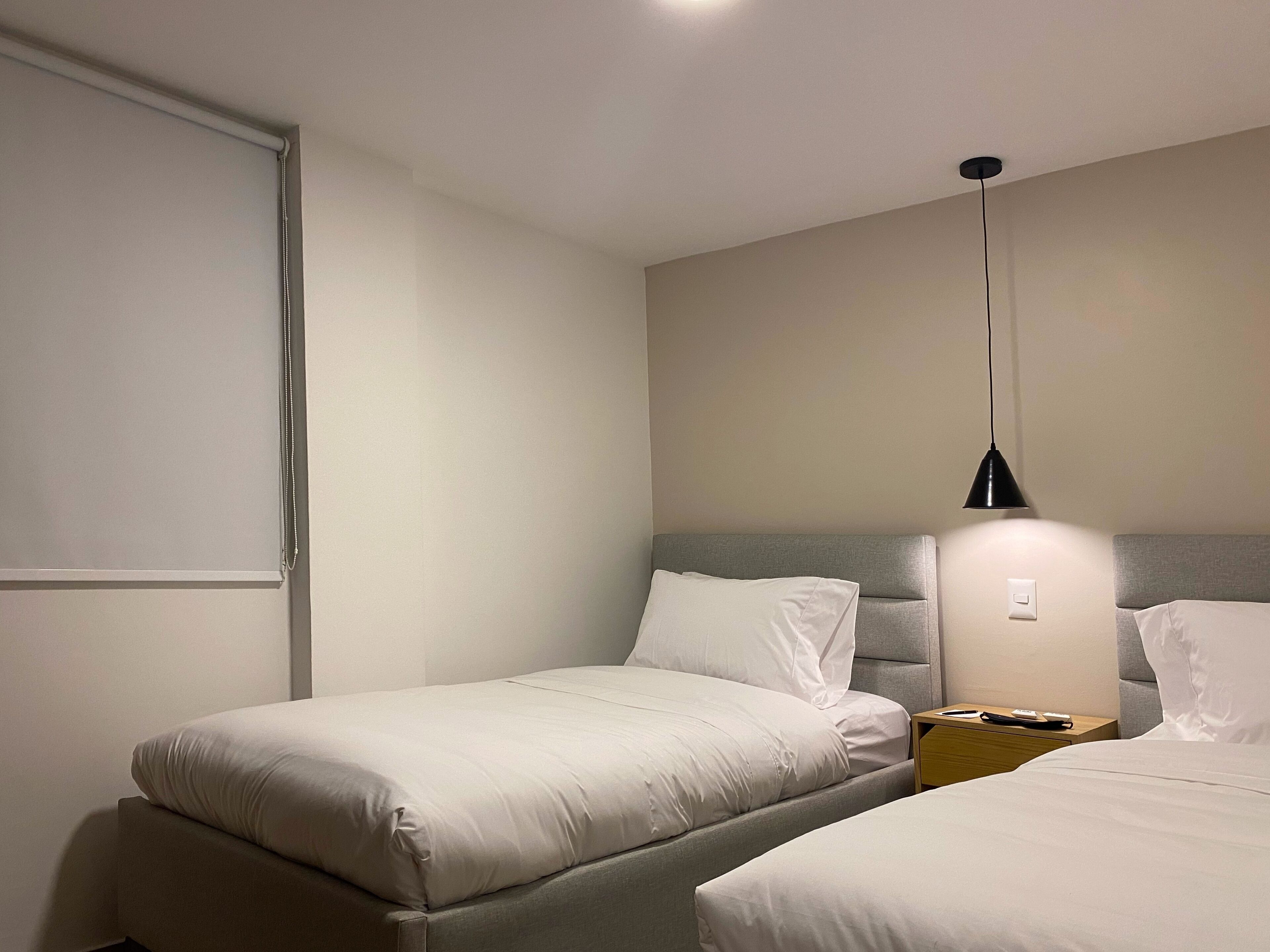 Ein Hotelzimmer mit zwei Betten, einem Nachttisch, einer Lampe und einem Fenster mit Jalousien.