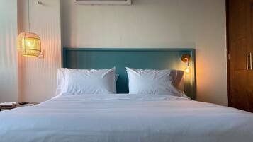 A neatly made bed with white linens, a teal headboard, and a wall-mounted air conditioner above it.