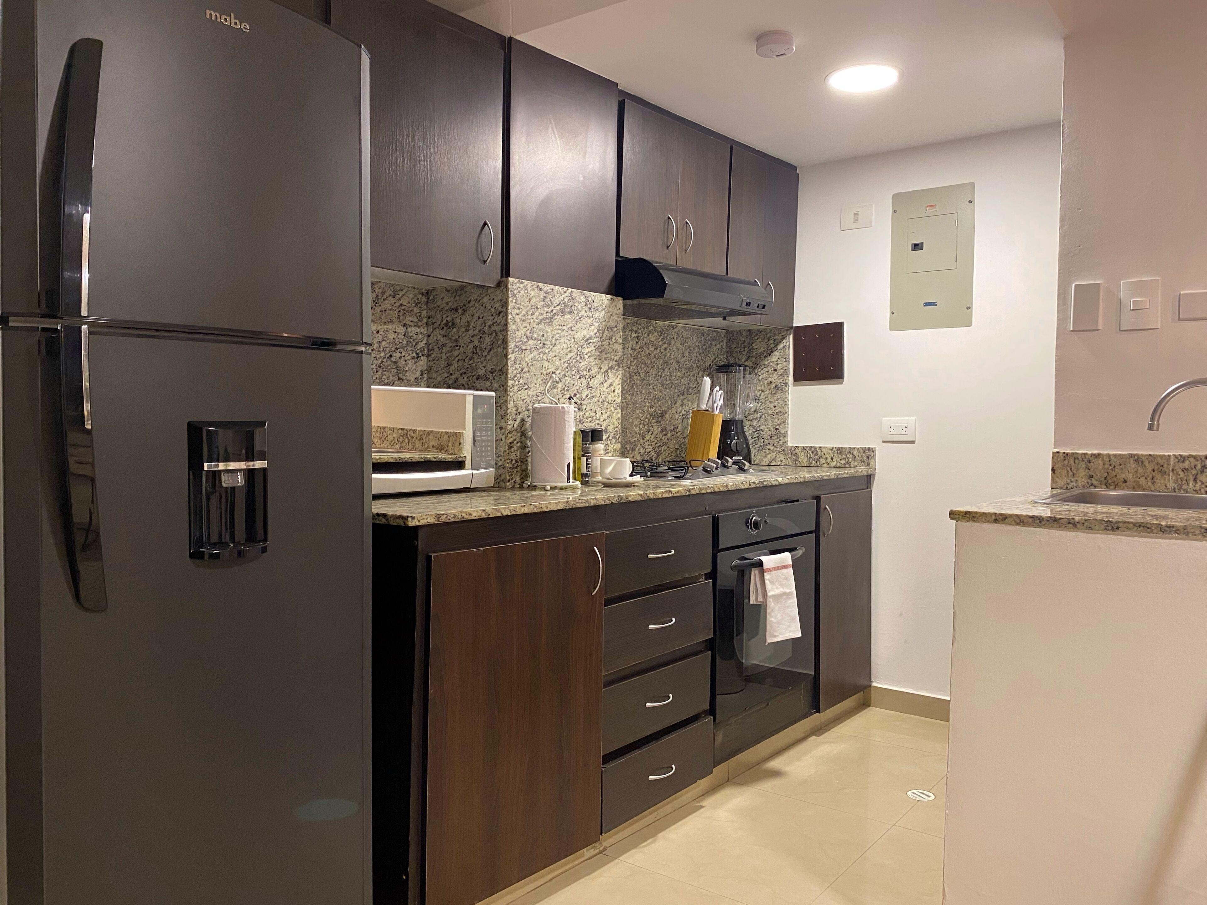 A modern kitchen with dark wood cabinets, a stainless steel refrigerator, a microwave, and a built-in oven.