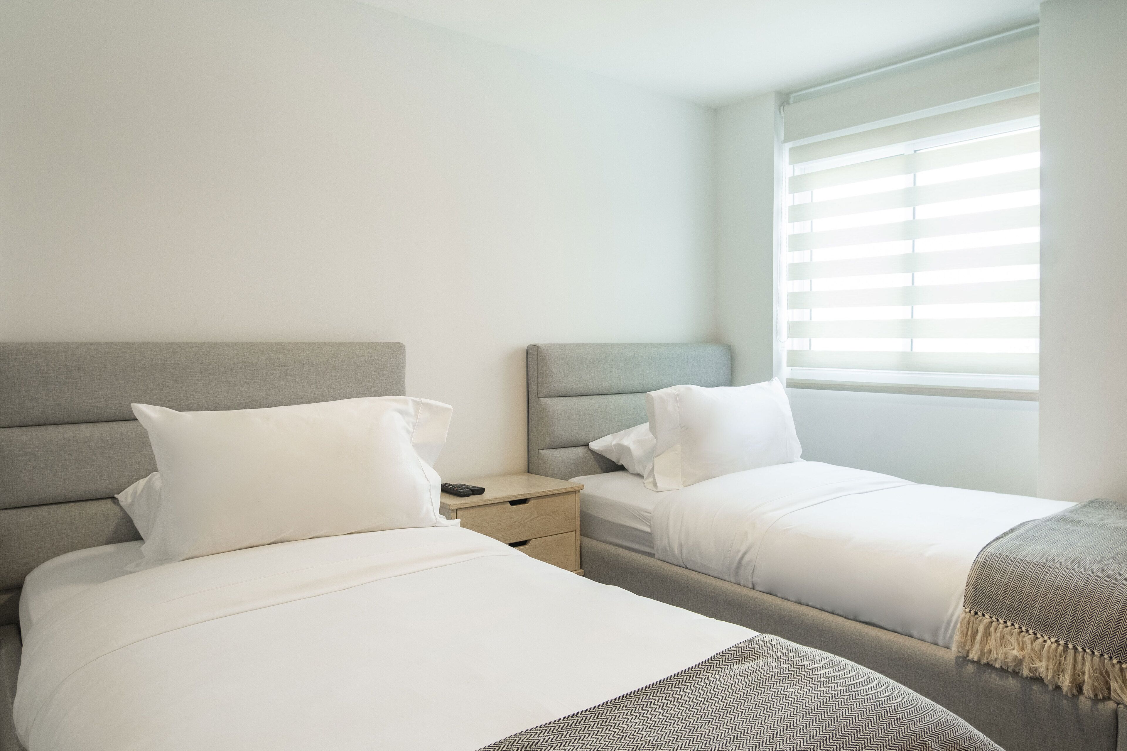 A hotel room with two beds, a nightstand, and a window with blinds.