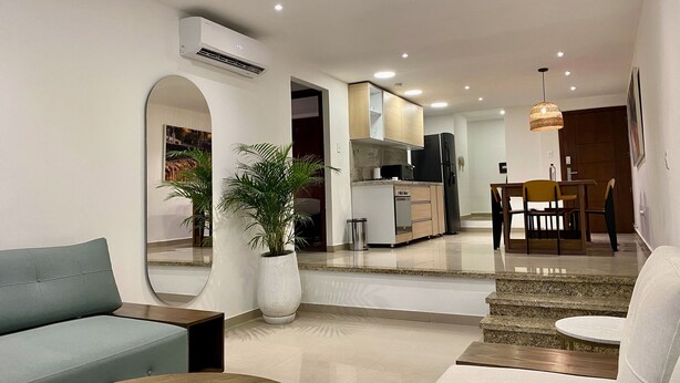 A modern living room with a sofa, a coffee table, and a potted plant. There is a kitchen area with a dining table and chairs. - Minarete By Wynwood House  (Cartagena)