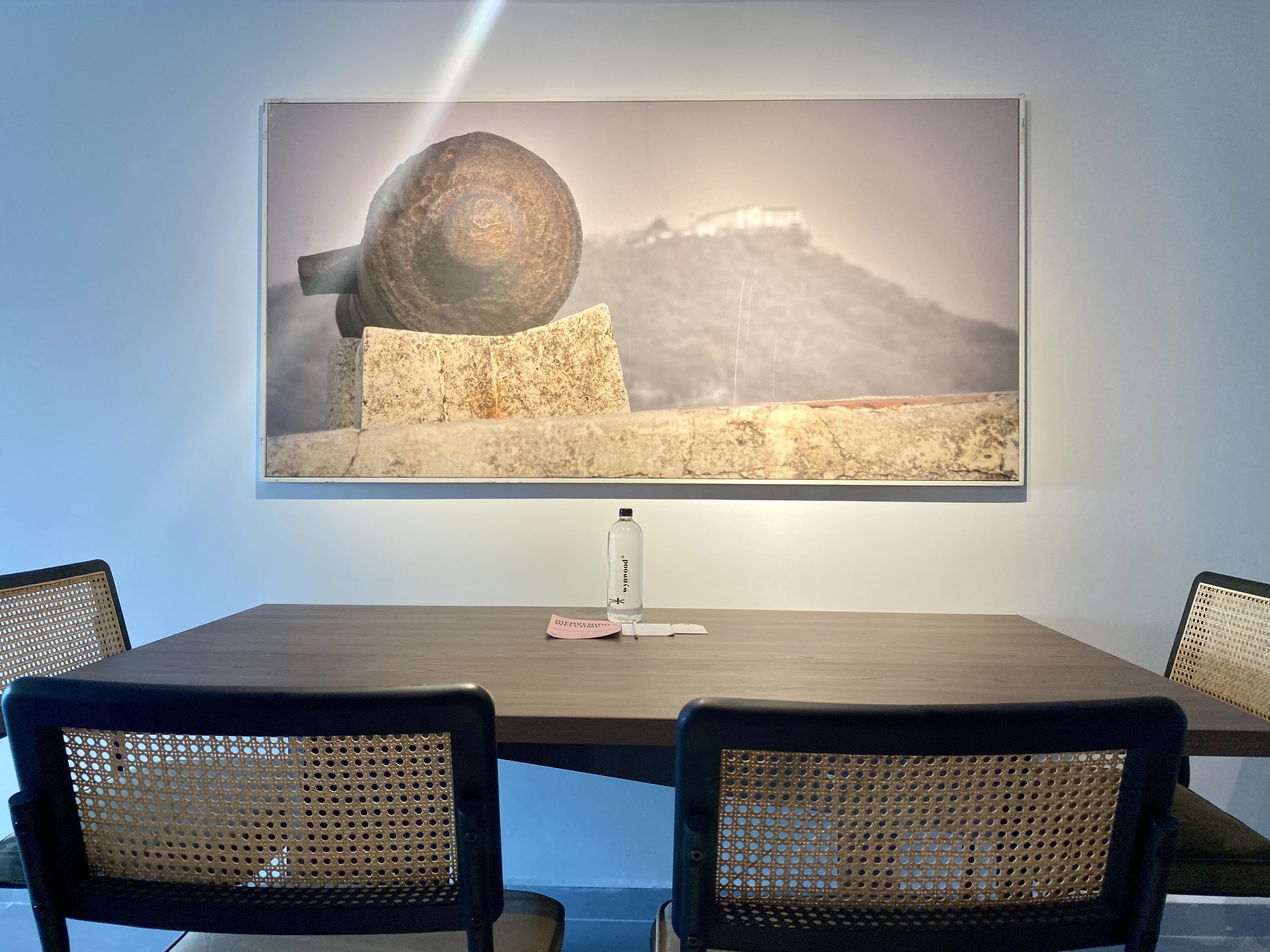 A dining table with two chairs, a bottle, and a framed picture on the wall.