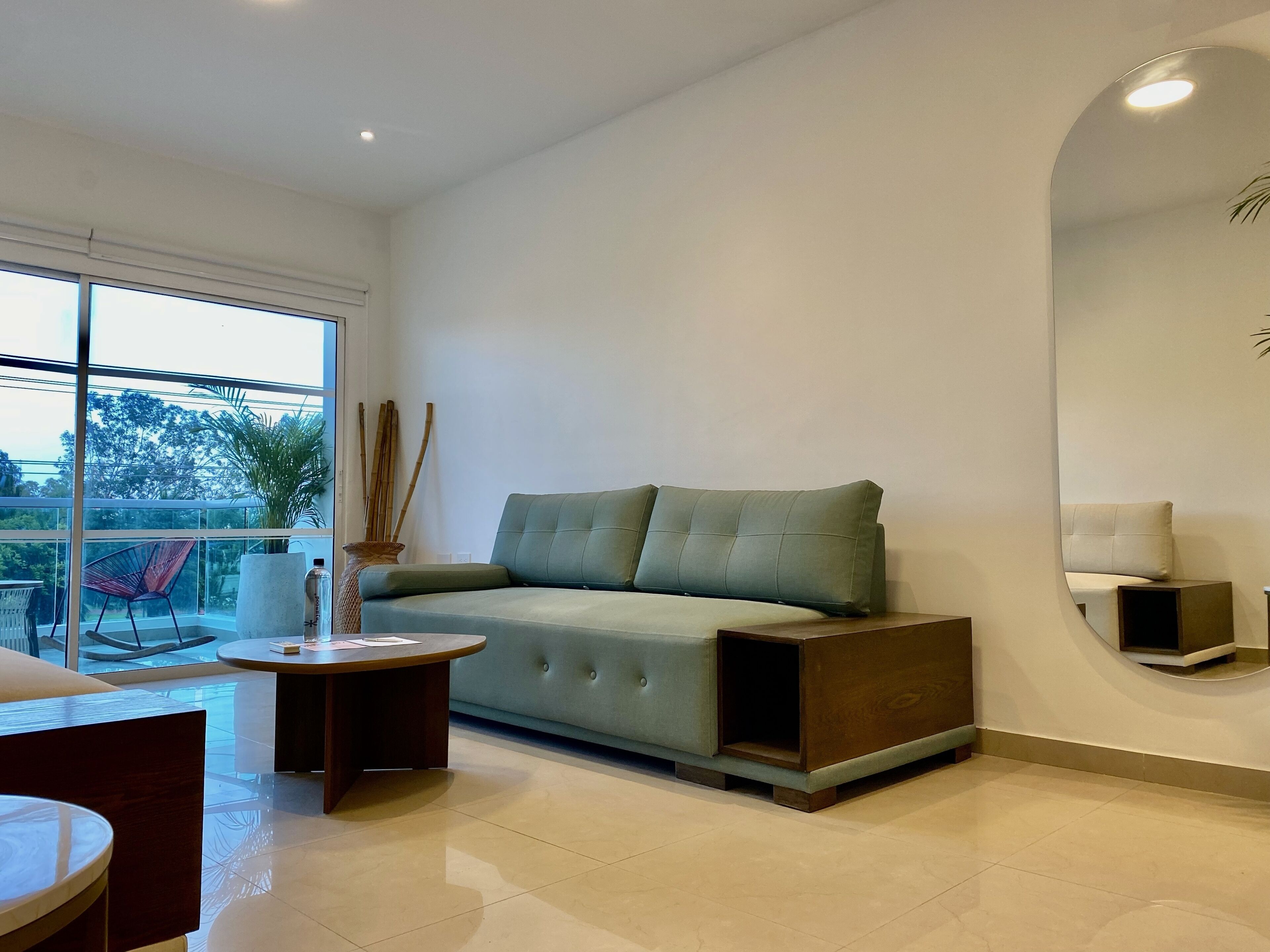 A modern living room with a green sofa, a round coffee table, and a large window offering a view of the outdoors.